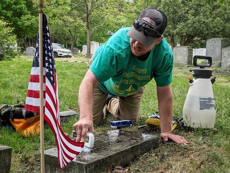 Man cleans moss and lichen off a grave stone in a cemetery